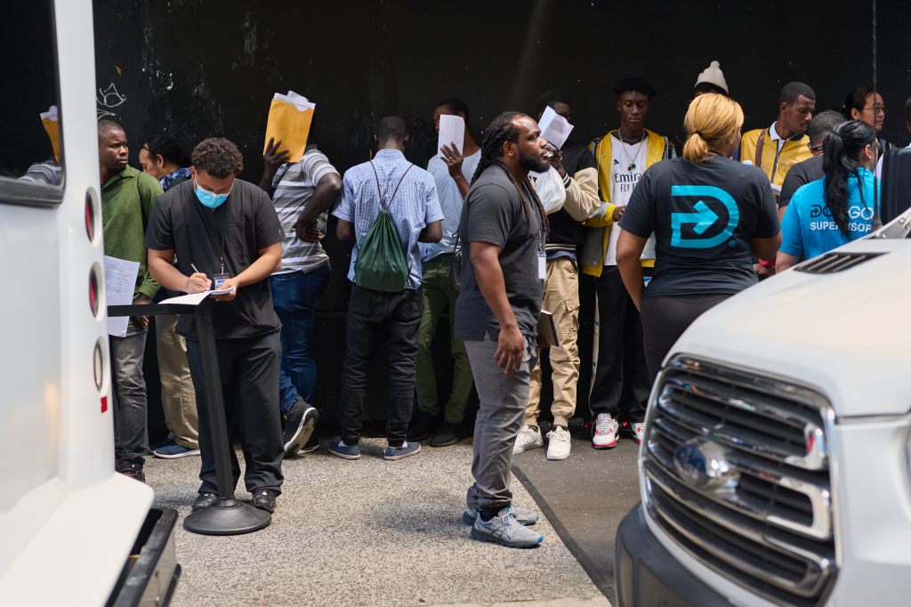 Asylum seekers lined up on E. 45th Street outside The Roosevelt Hotel, with some being attended to by DocGo mobile medical service personnel