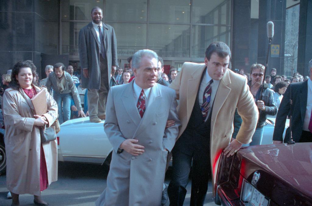 Reputed Mafia boss John Gotti is escorted by an unidentified man through the crowds during his trial