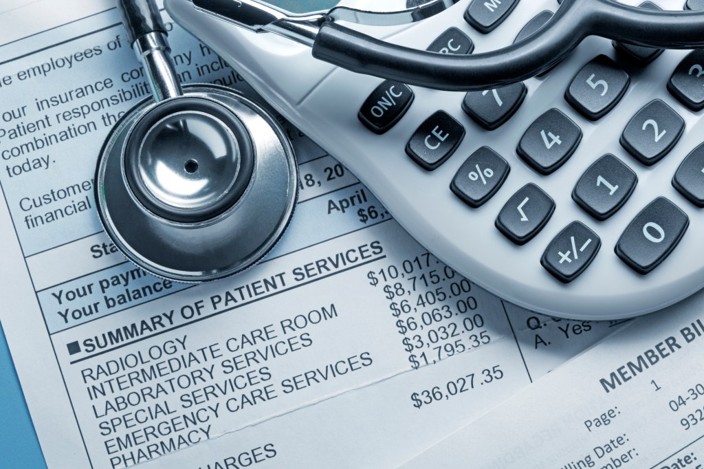 A stethoscope and a calculator rest on top of a medical bill.