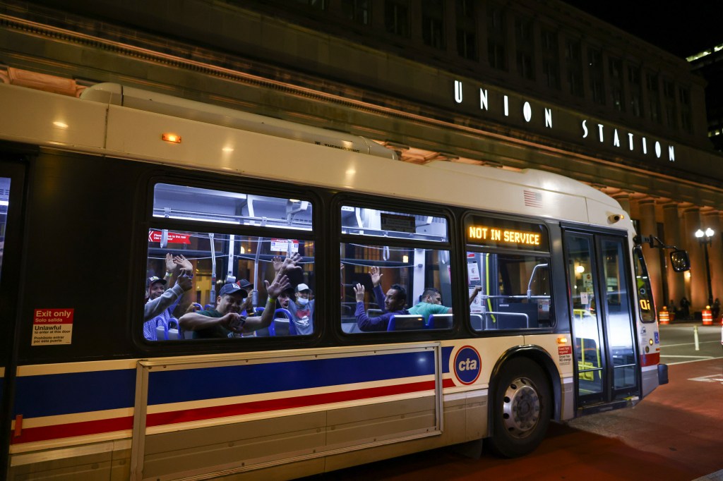 Migrants wave as the bus they are heads to a refugee center in Chicago on Aug. 31.