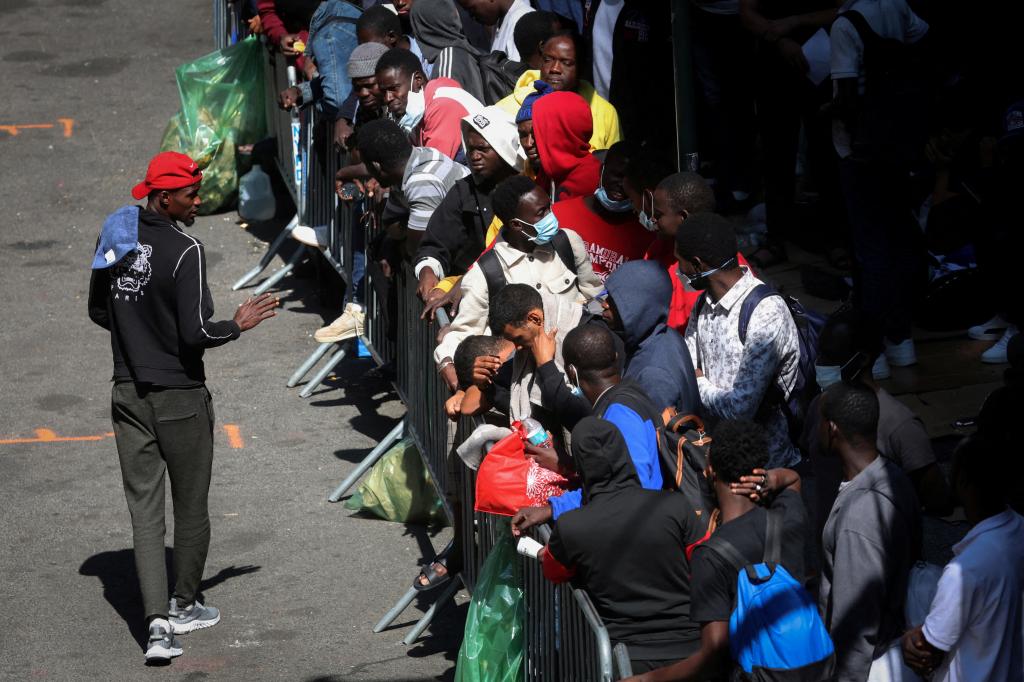 Recently arrived migrants to New York City wait on the sidewalk outside the Roosevelt Hotel in midtown, Manhattan.