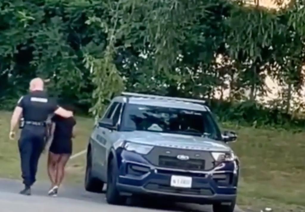Marlett walks with his arm around Pinto before helping her into his squad car in a parking lot near a park full of children