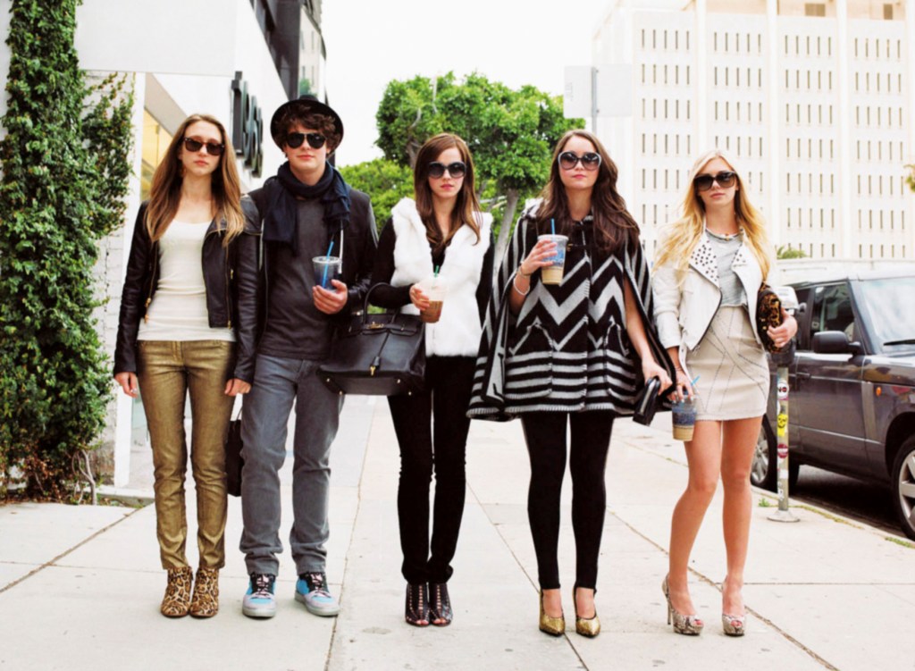 Emma Watson and the cast of "The Bling Ring" walking outside on the street wearing designer clothes.