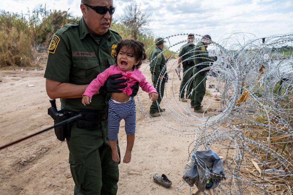 A U.S. Border Patrol agent holds a child from Venezuela as her parents cross through razor wire at the U.S.-Mexico border on September 27, 2023 in Eagle Pass, Texas. 