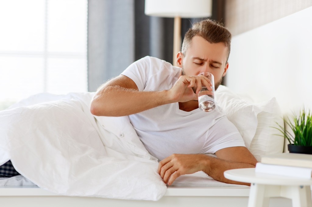 Photo of a man drinking water in a white bed