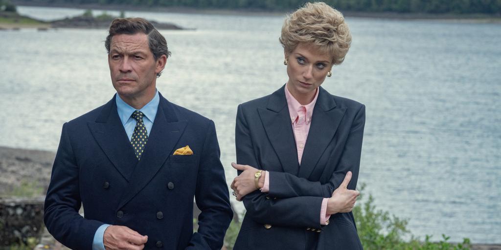 Dominic West as Prince Charles and Elizabeth Debicki as Diana Princess of Wales standing by water looking stern. 