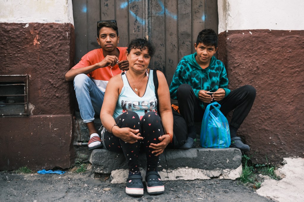 Migrant Beibis Roman and two of her three children sitting on a stoop in Ecuador