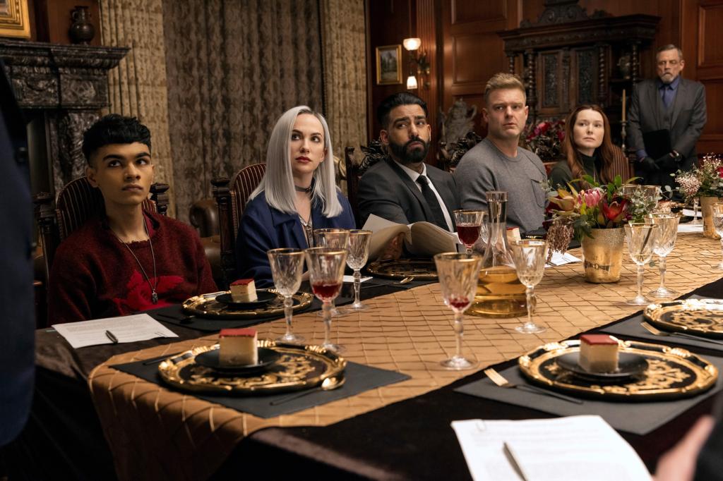 Sauriyan Sapkota, Kate Siegel, Rahul Kohli, Matt Biedel, Samantha Sloyan and Mark Hamill in "The Fall of the House of Usher" sit behind a table looking serious. 