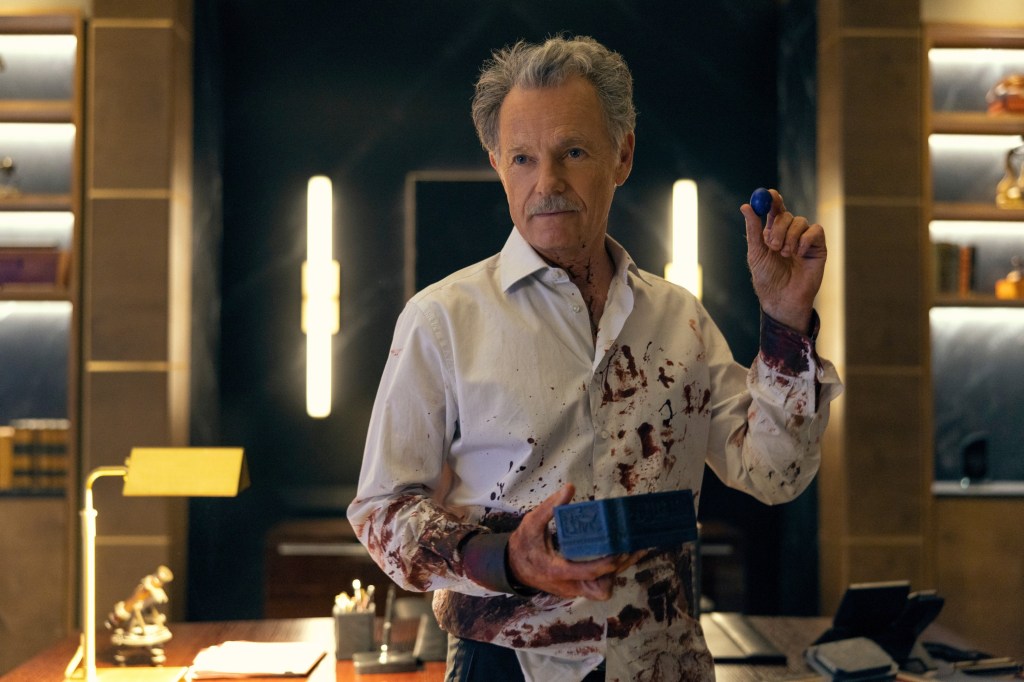 Bruce Greenwood as troubled patriarch Roderick Usher, holding a box, with blood spatter on his shirt. 