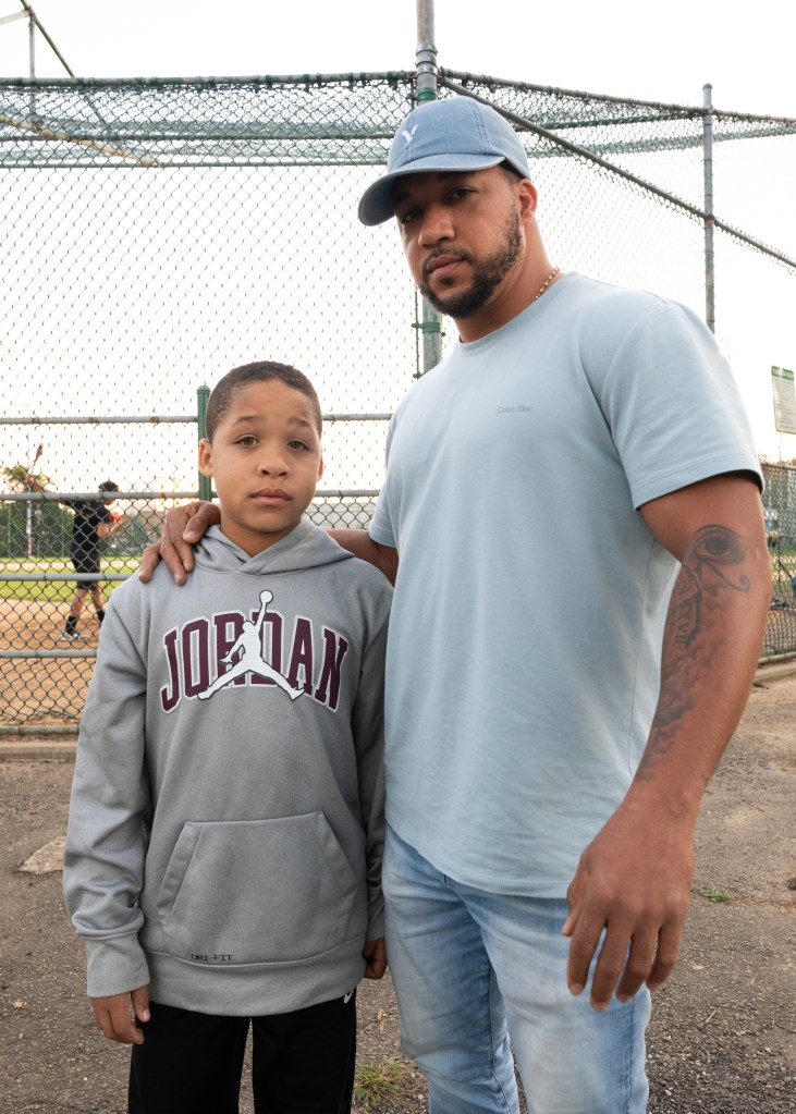 José Luis Peña poses with his son in front of baseball field