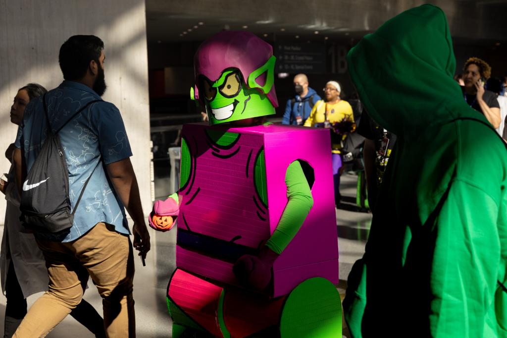 a person in a green and purple costume made from boxes walk through a crowd