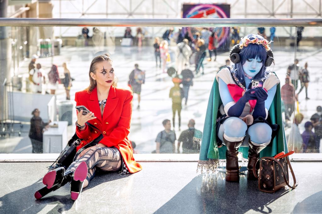 two women in costumes sit on the floor and checking their phones