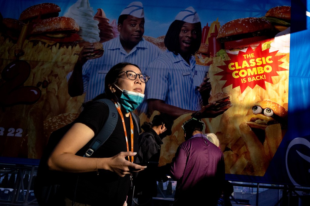 a woman looks up from her phone as she passes a large billboard at comic con