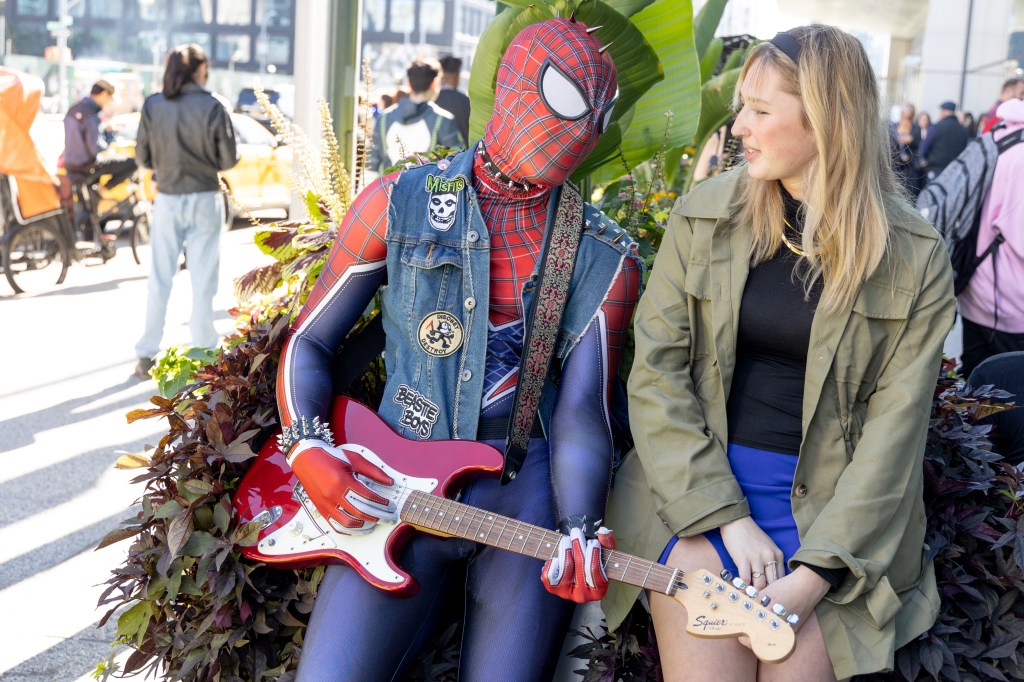 a man dressed as spider man holding a guitar sits next to a woman in costume