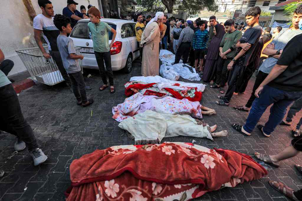 People gather Wednesday by the covered bodies of victims who died in an overnight blast at the Ahli Arab hospital in central Gaza.