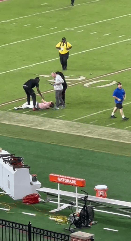 The fan lies down on the field after a big tackle from a security guard on the field.