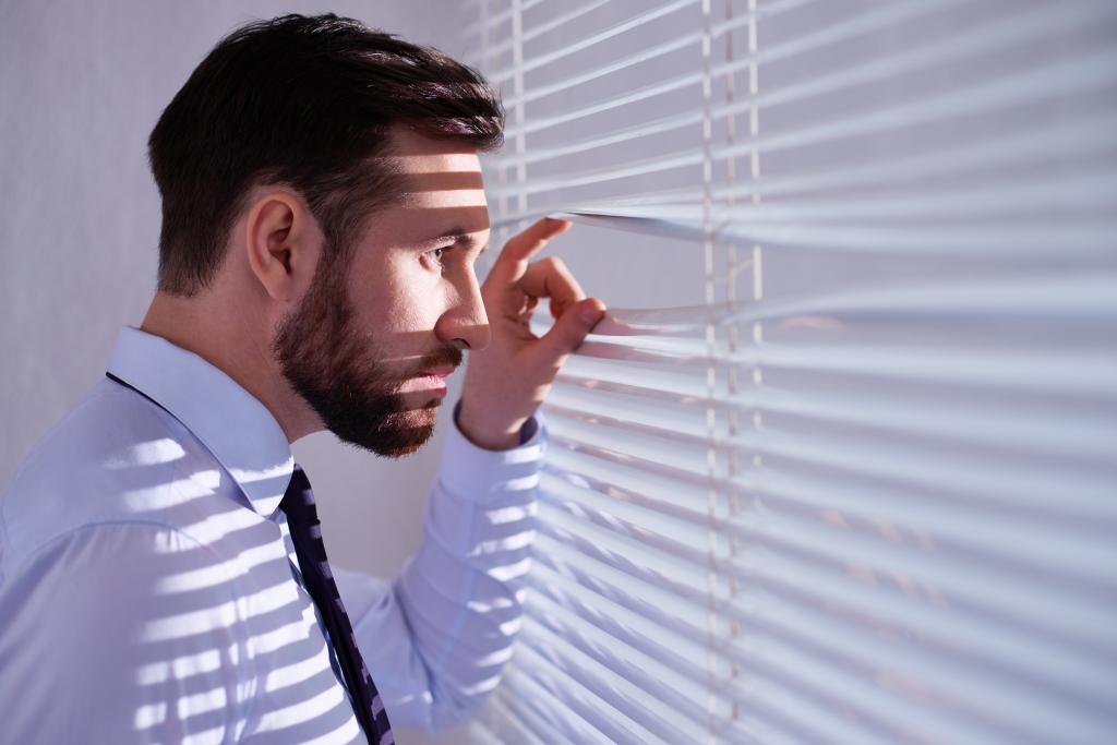 Serious businessman peeking through blinds