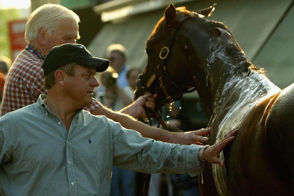 Trainer John Servis helps steady Smarty Jones while stable manager Bill Foster holds the lead, as the colt gets bathed following his morning workout in preparation for the 129th running of the Preakness at Pimlico Race Track on May 14, 2004 in Baltimore, Maryland. 