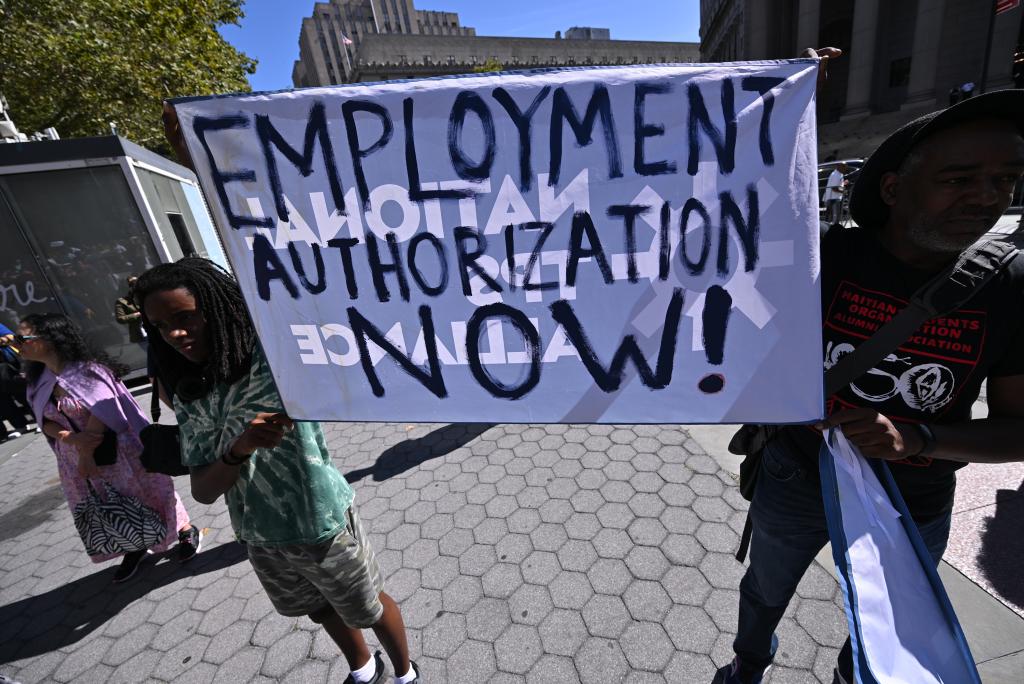 People hold a sign reading "employment authorization now"