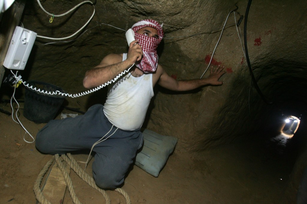 A masked Palestinian man speaks by telephone with his colleagues at the Egyptian side as he and others (not pictured) smuggle food, milk and supplies underground June 27, 2008 in a tunnel, which links between Rafah southern Gaza Strip and Egypt.