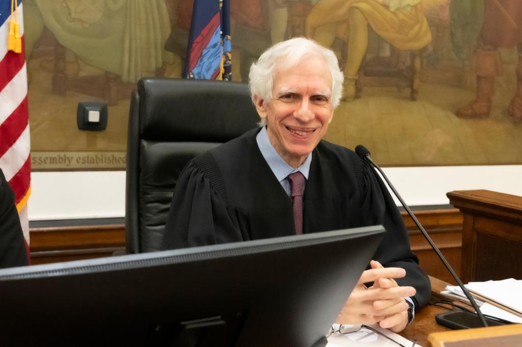 Manhattan Supreme Court Justice Arthur Engoron seated at the bench in court in his judges robe with a large mural on the wall behind him.