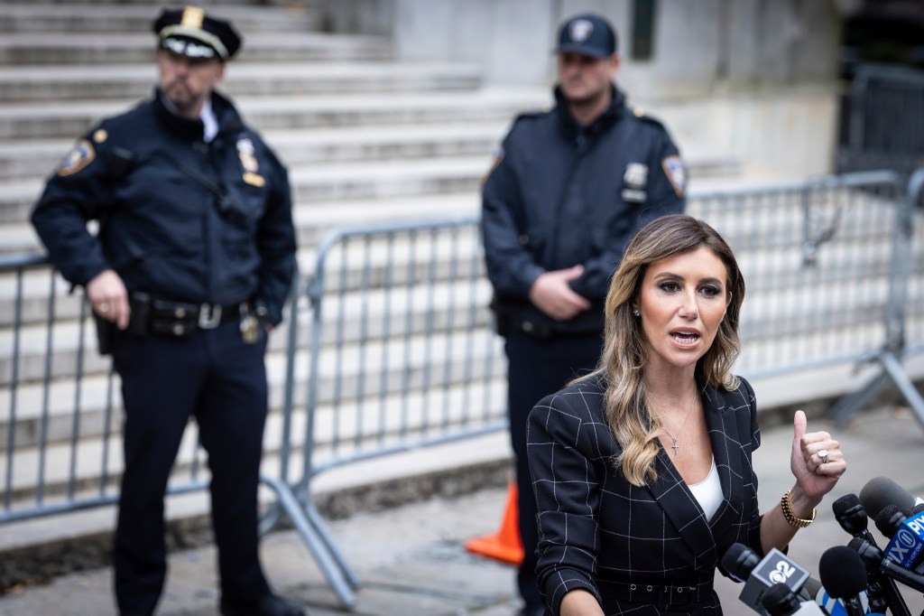 A woman in a business suit talking into microphones in front of courthouse steps with two male uniformed NYPD officers standing behind her.