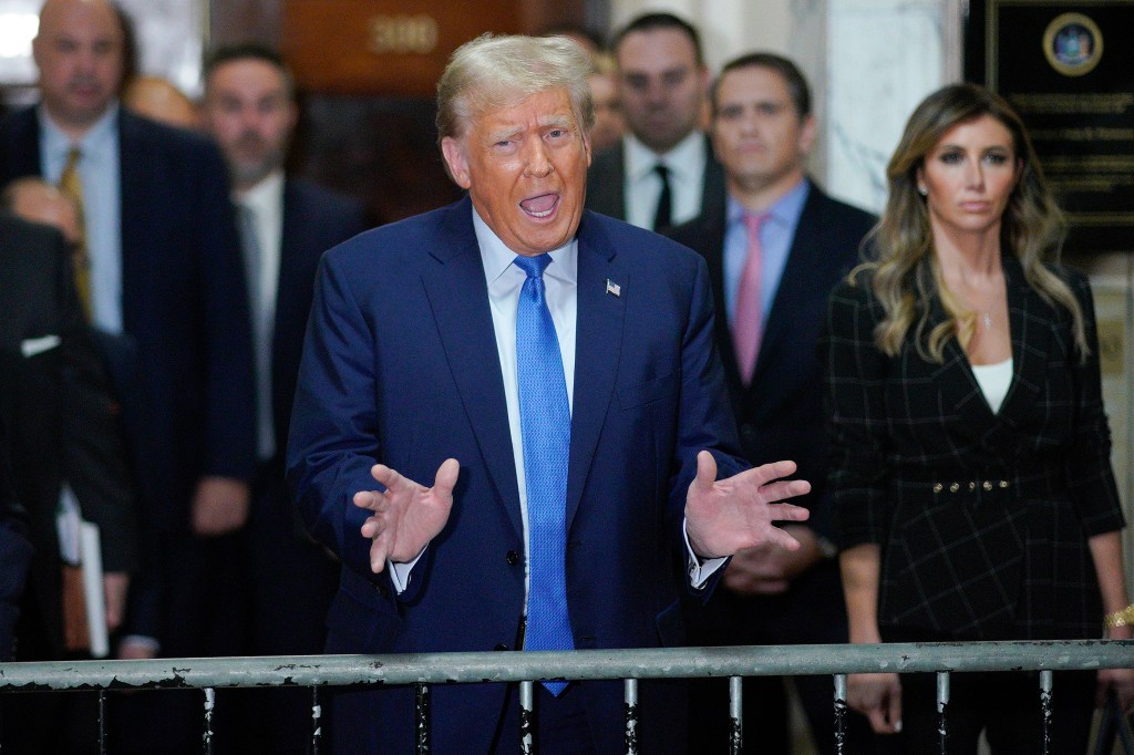 Former President Donald Trump gesturing with his hands while speaking to reporters with his legal team and other onlookers standing behind him.