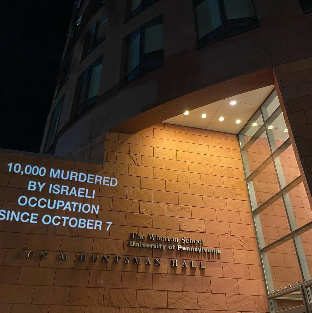 A slogan beamed onto a wall of a building at UPenn, reading, "From West Philly to Palestine, occupation is a crime."