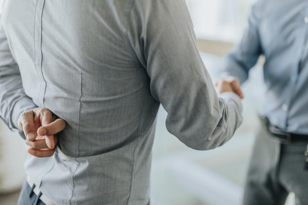 Close up of unrecognizable businessman holding his fingers crossed while shaking hands with his colleague.