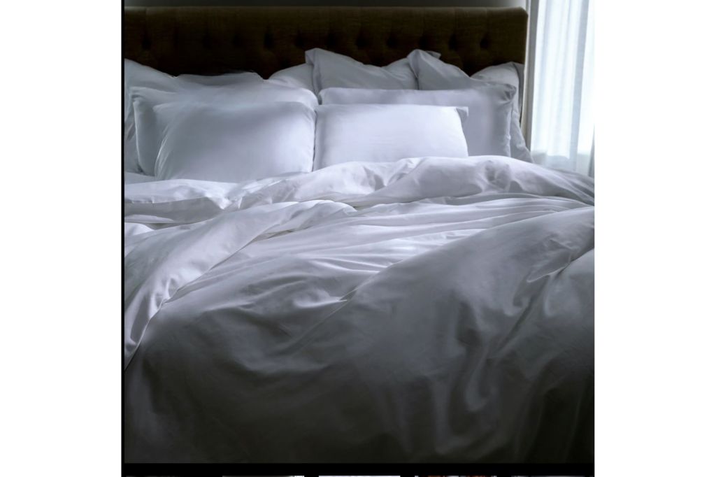 An unmade bed with white pillows, sheets and duvet covered.