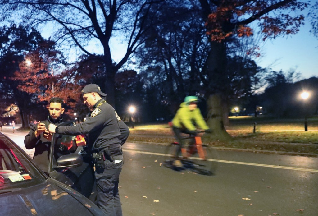 Police investigate a shooting inside Prospect Park as a person bikes by. 