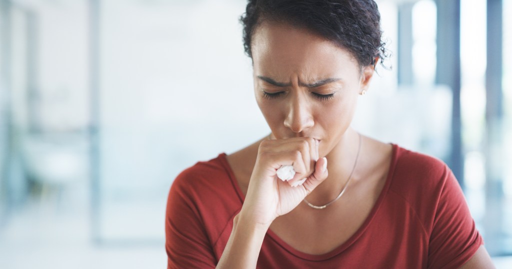 Cropped shot of an attractive young businesswoman sitting alone in her office and coughing as she suffers from a cold