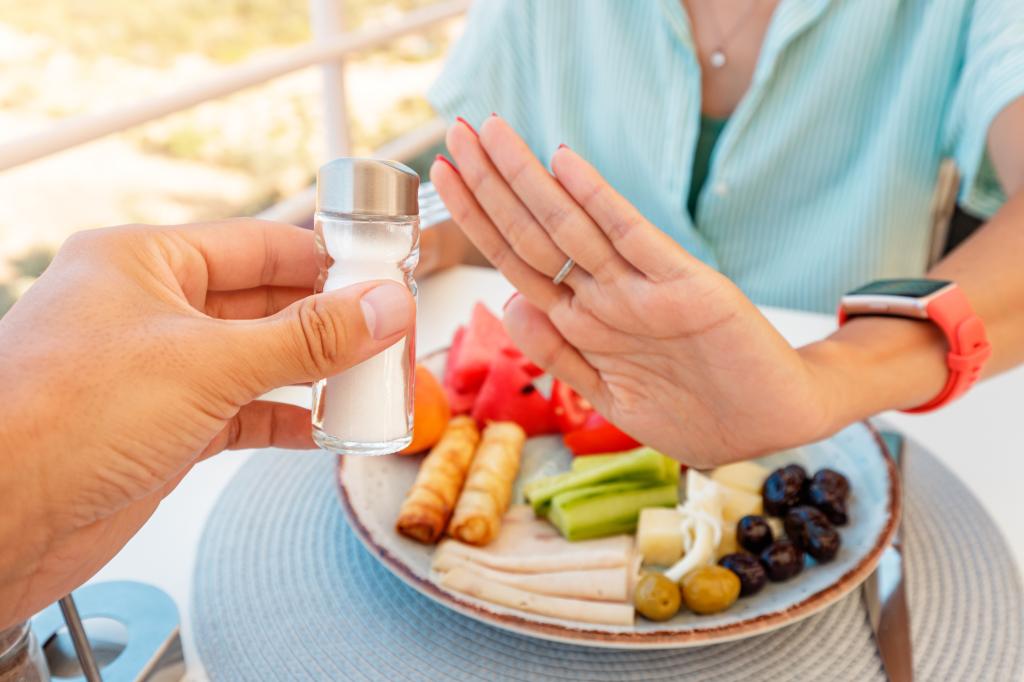 Woman in a restaurant refuses the offered salt and pepper shaker with a gesture of her hand. 