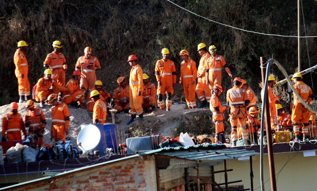 More than 20 rescuers wearing orange jumpsuits rest at the site of an under-construction road tunnel that collapsed.