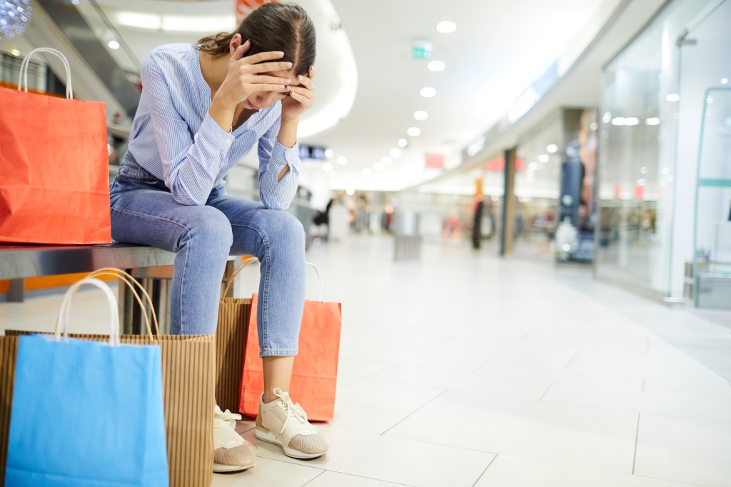 Woman in the mall with head in hands surrounded by shopping bags