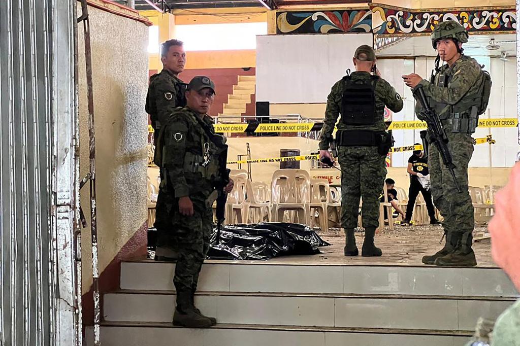 Military personnel stand guard at the entrance of a gymnasium while police investigators