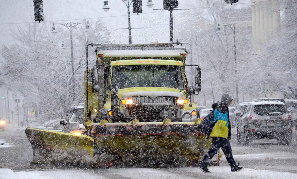 A pedestrian passes a snowplow in Pittsfield, Mass., Wednesday Dec. 10, 2014.  A nor'easter has brought mixed precipitation to the region. A winter weather advisory remains in effect for the Berkshires. (AP Photo/The Berkshire Eagle, Ben Garver)