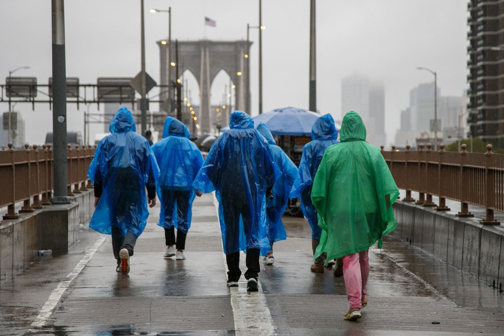 People walk across Brooklyn Bridge in the rain, seen from behind in ponchos.