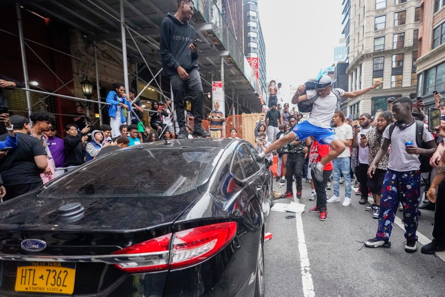 A demonstrator kicks a car window near Union Square Park on Friday, Aug. 4, 2023, in New York as police struggle to control a crowd of thousands who gathered in Manhattan for online streamer Kai Cenat's videogame console giveaway that got out of hand. 