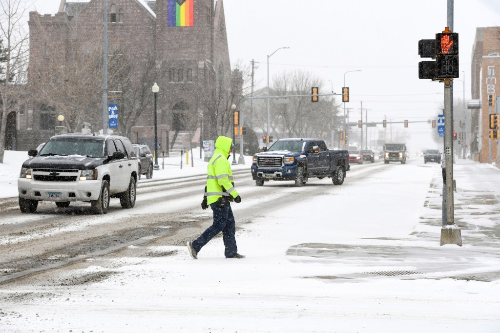 A pedestrian walks across town as the first snow falls ahead of a winter storm on Tuesday, Feb.  21, 2023, in Sioux Falls, S.D. A wide swath of the Upper Midwest is bracing for a historic winter storm. The system is expected to bury parts of the region in 2 feet of snow, create dangerous blizzard conditions and bring along bitter cold temperatures.   (Erin Woodiel /The Argus Leader via AP)