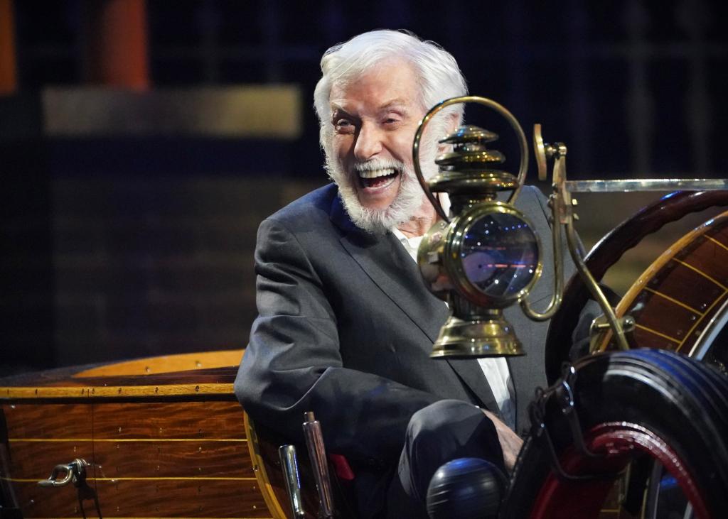 Dick Van Dyke sits in the car from "Chitty Chitty Bang Bang" in the CBS special celebrating his movie and television career. He's grinning broadly as he looks off-camera.