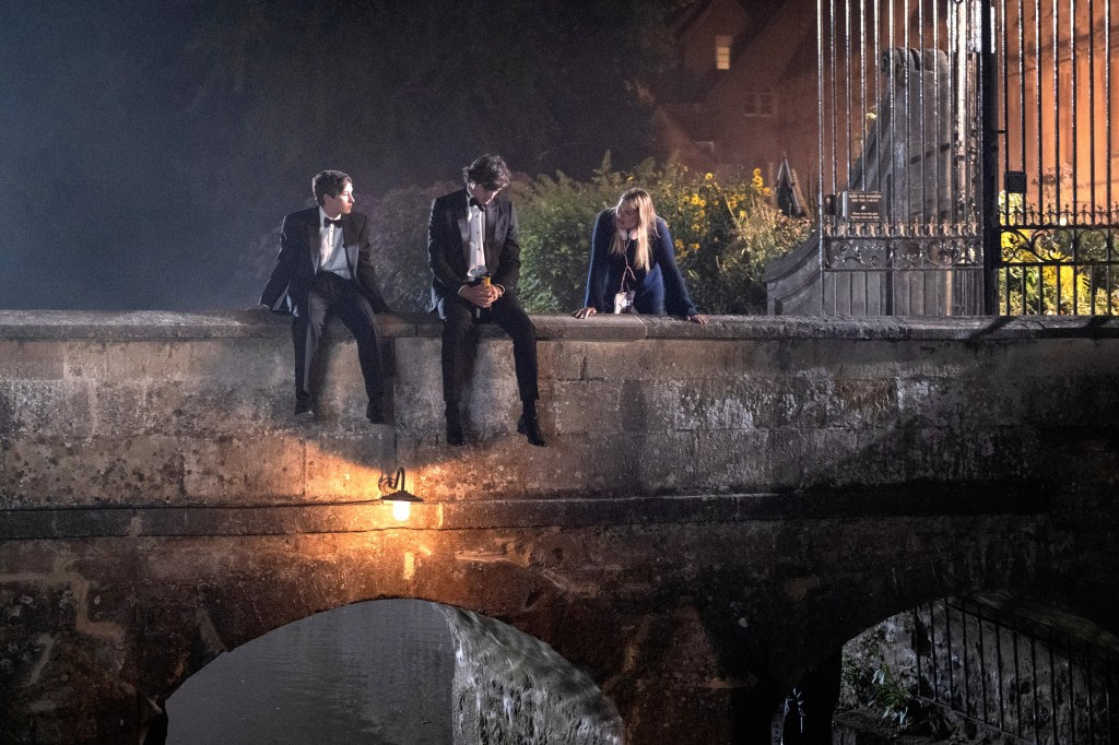 Barry Keoghan, Jacob Elordi and director Emerald Fennell sitting on a bridge. 