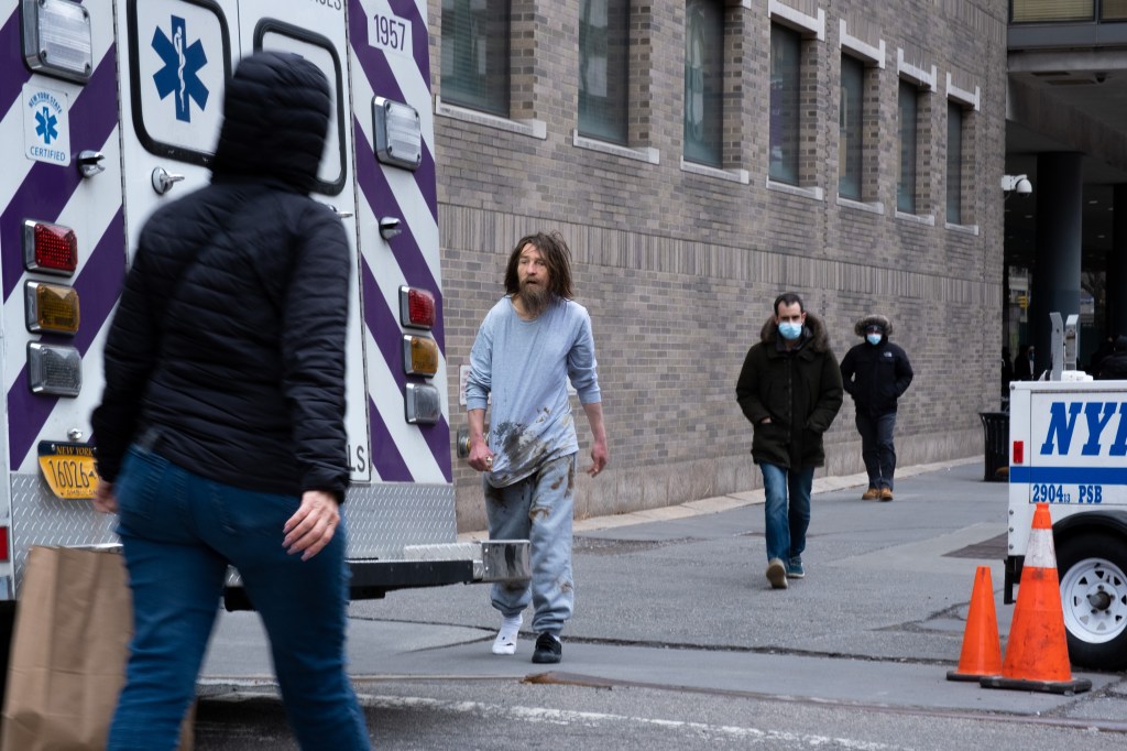 A homeless man walks by an ambulance. 