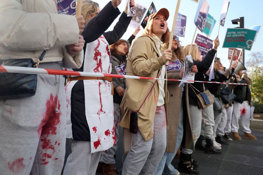 Women wearing clothes with fake blood at a protest waving signs