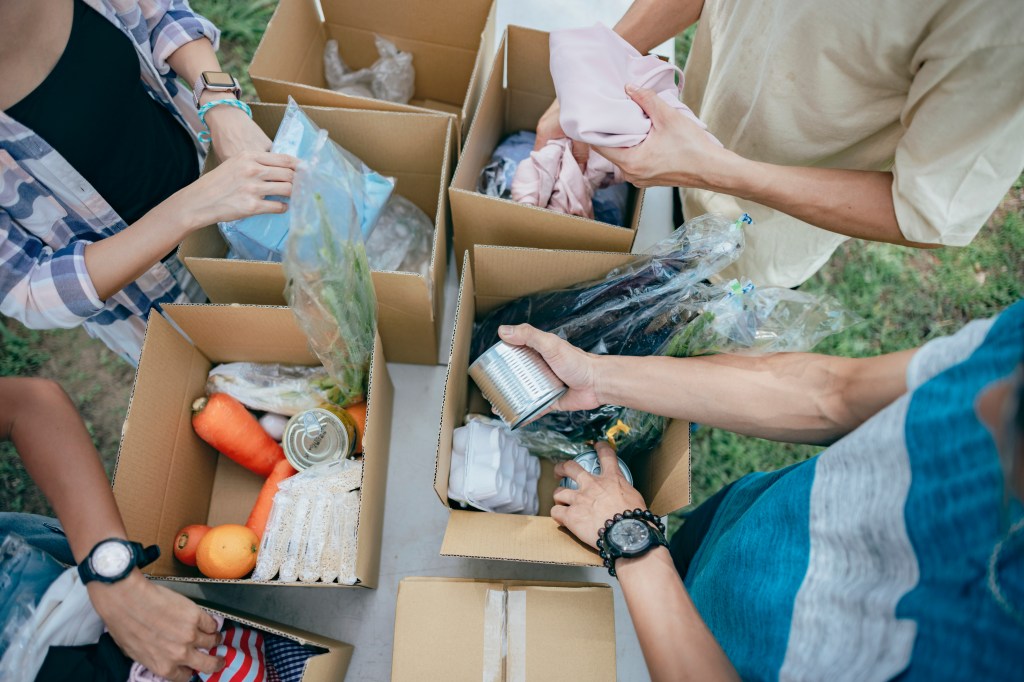 A group of young Asian volunteers preparing grocery food into boxes for those needy people having financial difficulty during global economy crisis. Food box filled with fresh vegetables, fruits, cereals, milk, eggs and canned goods are deliver to the local needy community during a outdoor food drive.