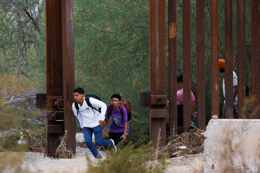 Migrants run through wide-open monsoon gates at the border wall near Lukeville, Ariz., on Aug. 20, 2023.