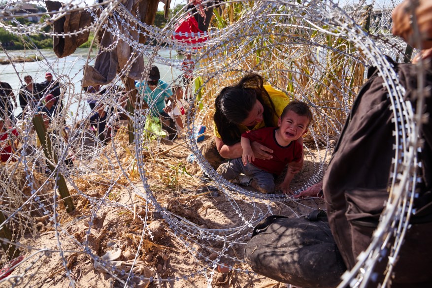 A mother from Honduras crawls through razor wire with her three children after crossing the Rio Grande river from Mexico into the United States on Sunday, September 24, 2023 in Eagle Pass, Texas.