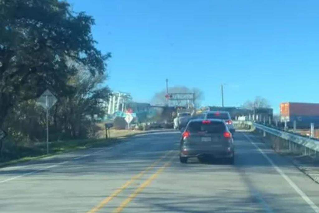 Video shows a man sitting in a car when a train crashes into a semi-truck at full speed. 