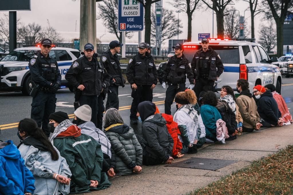 Detained anti-Israel protesters sit in a line along a road as they await for transportation from the Port Authority Police.