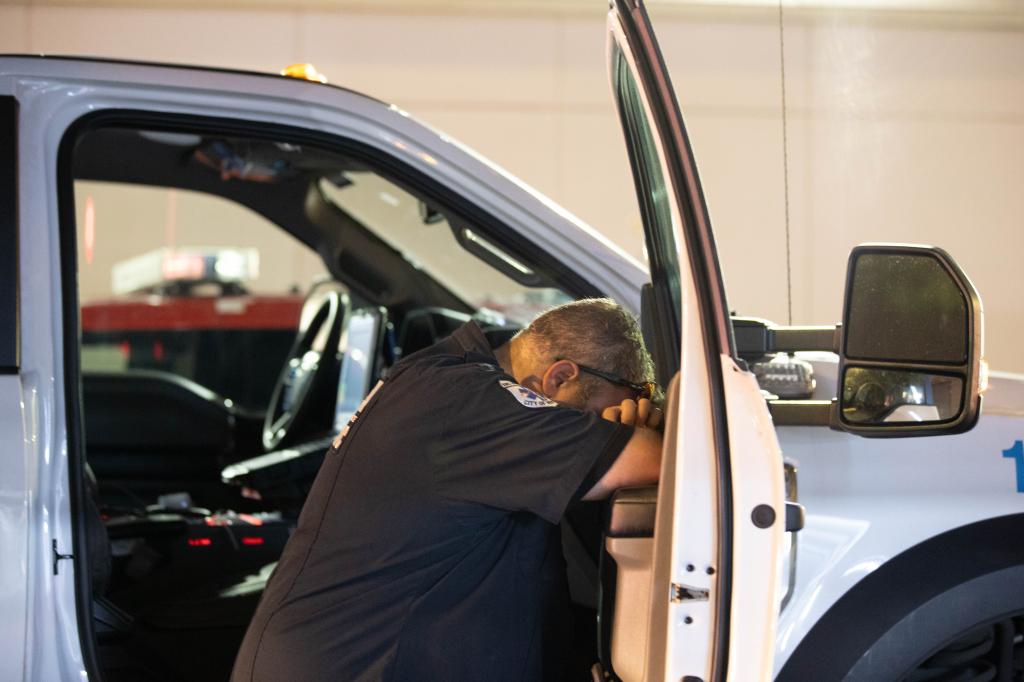 An exhausted EMS worker rests his head in his arms on the door of an ambulance.